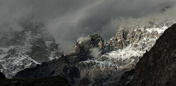 This photograph captures the tumultuous beauty of the Karakoram’s peaks, where clouds and mountains engage in an eternal dance. Light breaks through the overcast sky, spotlighting the rugged cliffs and snow-dusted crevices, embodying the raw power of nature’s artistry. The scene invites viewers to listen for the whispers of the wind that sculpts these giants—a symphony of natural forces at play.