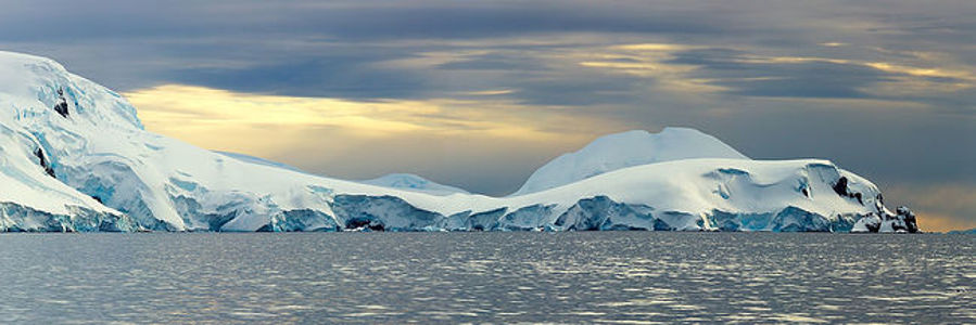 The tranquil waters of the polar sea reflect the soft glow of twilight, framing the majestic ice formations along the horizon. This panoramic image showcases the subtle interplay of color and light in the Antarctic wilderness, where the serene blues and whites of the ice contrast with the darkening sky. A testament to the quiet majesty of the Earth’s southernmost landscapes, it is a serene backdrop for contemplation and a splendid addition to any art collection.