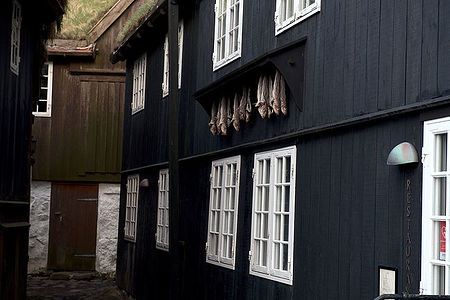 This image presents a close-up view of the iconic black-tarred wooden houses in the Faroe Islands, adorned with white windows and drying fish, a testament to the islands’ fishing heritage. The grass roofs blend into the environment, displaying the unique cultural and architectural tradition of this remote archipelago.
