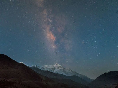 The night sky, embroidered with the Milky Way, serves as a celestial canopy over the Annapurna massif. This image captures the silent watch of the mountains under a universe brimming with stars, showcasing a night where nature and the cosmos converge.