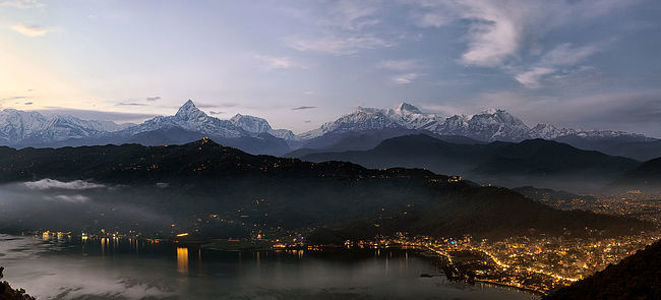 As dusk falls, the vibrant city of Pokhara is illuminated beneath the towering Annapurna range. This image captures the tranquil fusion of urban lights with the natural splendor of the Himalayas, reflecting a unique blend of human settlement and wild beauty.