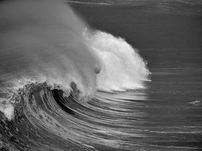 Суровые монохромные тона этой фотографии подчеркивают мощь и сложную текстуру волны в момент ее обрушения. Брызги, застывшие в неподвижности на фоне темной воды, создают драматическую и неподвластную времени морскую сцену.