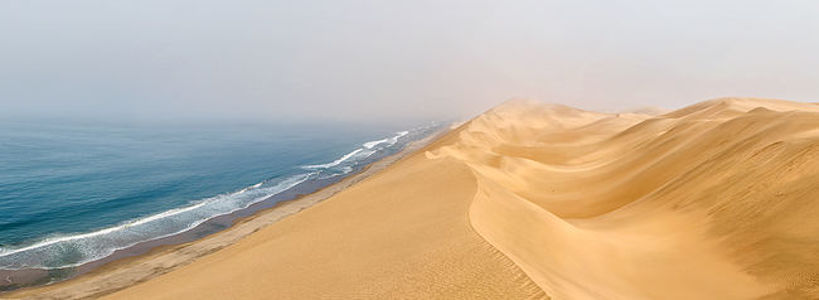 На этом снимке красиво контрастируют размашистые золотые дюны пустыни и безмятежная синева океана. Сцена, в которой сходятся эти два огромных и разных ландшафта, символизирует красоту природы и гармоничное сосуществование контрастных элементов.