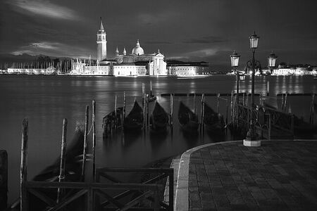 Испытайте тихую красоту ночной Венеции с этим черно-белым изображением острова Сан-Джорджо Маджоре, отражение которого танцует на спокойных водах.