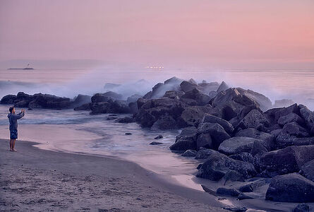 As twilight paints the sky in shades of purple and pink, a lone individual captures the serene beauty of the Los Angeles coastline. The misty waves gently crash against the rocks, creating a symphony of natural tranquillity.