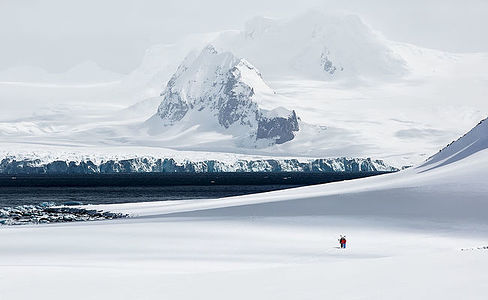 Against the immense canvas of Antarctica, two figures press forward, their presence a bold statement of life and exploration in this icy expanse. They are a vital reference point, offering a sense of scale to the endless white that stretches to the horizon. Their colorful gear stands out, a testament to the resilience and spirit of adventure that drives humans to explore even the most remote corners of our planet.