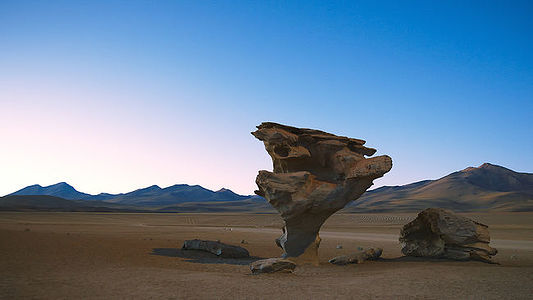 The ’Arbol de Piedra’, or Stone Tree, stands as an enduring testament to the sculpting forces of wind erosion in Bolivia’s Siloli Desert. Captured during the blue hour, the rock formation’s peculiar shape is highlighted against the twilight sky, with the Andean mountains providing a stark, distant backdrop. This natural monument, set in a desolate landscape, inspires awe with its resilience and artistry.