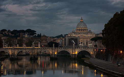 As dusk settles over Rome, the historic Ponte Sant’Angelo bridge leads the eye to the magnificent St. Peter’s Basilica, bathed in the gentle glow of twilight.