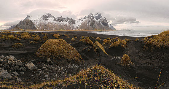 This art showcases the striking Vestrahorn mountain in Iceland, towering over the surrounding black sand dunes. The golden tufts of grass create a stark contrast against the dark volcanic sand, underlining the unique beauty of Iceland’s rugged coastline. The overcast sky hints at the challenging weather conditions, adding to the dramatic and natural allure of this remote landscape.