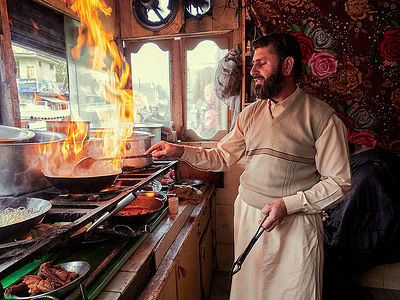 In the heart of Pakistan, a skilled chef masters the fiery dance of street cuisine. Surrounded by the vibrant ambiance of a local bazaar, he tends to sizzling pans over open flames. This photograph captures the essence of Pakistani culinary tradition, where the flame is not just a tool, but a central performer in the gastronomic experience.