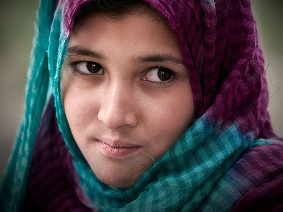 Portrait of a young girl with a striking gaze, draped in a vibrant turquoise and magenta scarf. Her eyes are a window to a soul.