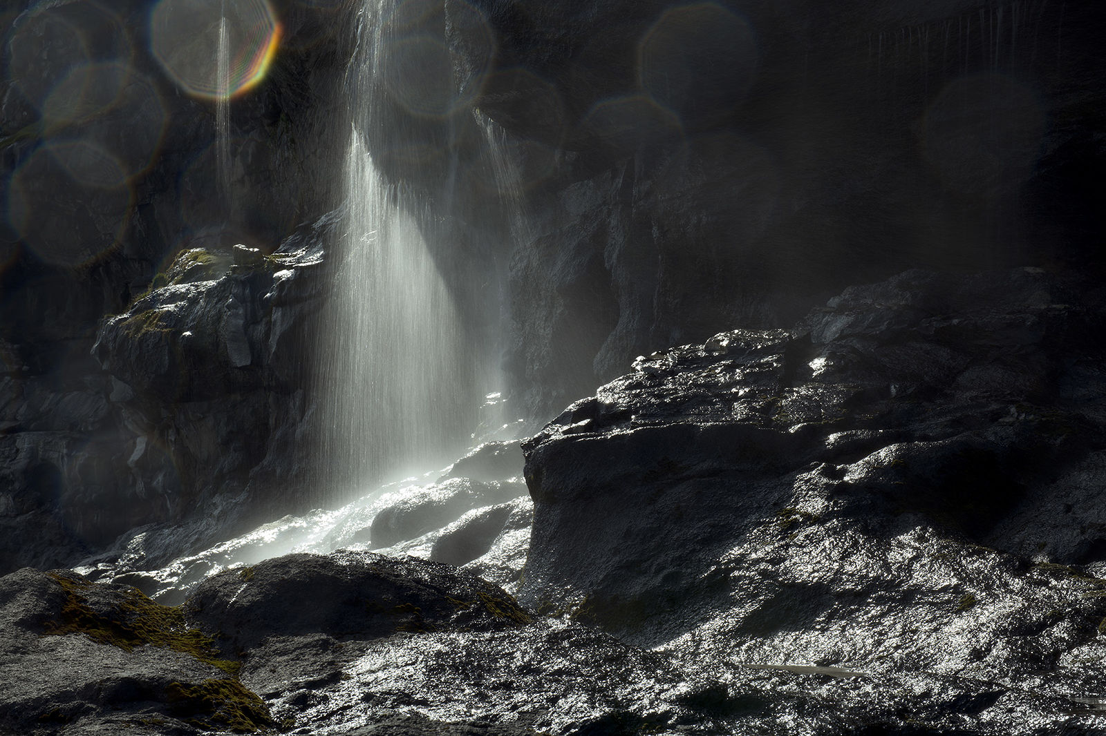 На этой работе показано неземная красота водопада на Фарерских островах, где солнечный свет проникает сквозь туман, создавая завораживающую игру света и тени на изрезанных скалах. Блики на объективе придают сцене мечтательный характер, подчеркивая чарующую игру природы.