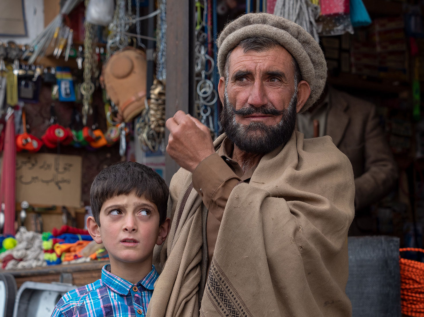 An authentic capture of a bearded elder in traditional attire with a young boy beside him, set against a backdrop of a local market, showcasing a moment of generational bonding and cultural richness.